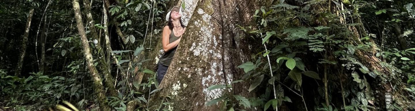 student Lena Wehn standing next to a tall tree in the Amazon rainforest in Ecuador 