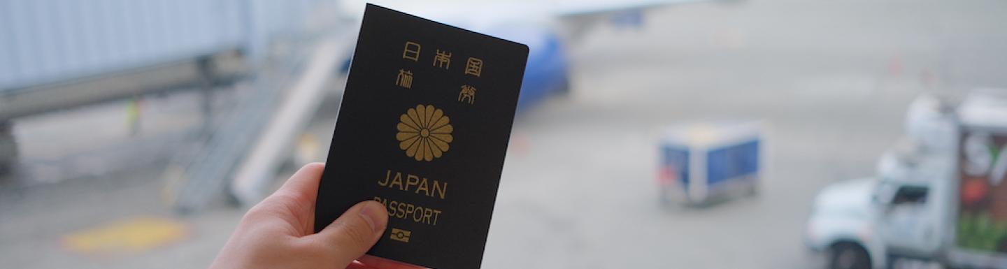 Photo of someone holding a passport in front of an airplane tarmac
