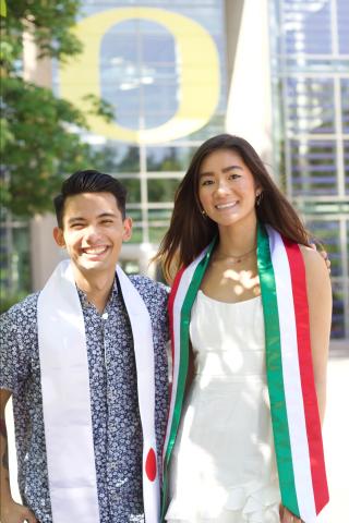 Two University of Oregon students wearing graduation sashes, one with the Mexico flag and the other with the Japan flag