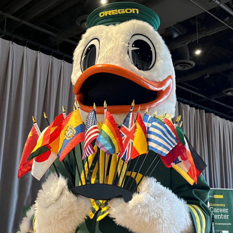 The Oregon Duck holding several small country flags