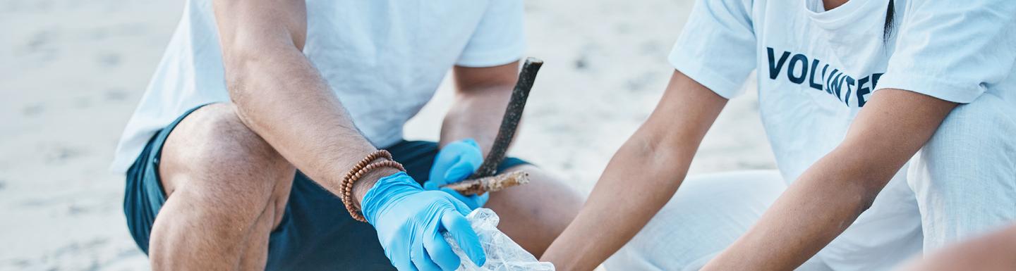 Volunteer, hands of people wearing plastic gloves cleaning beach 