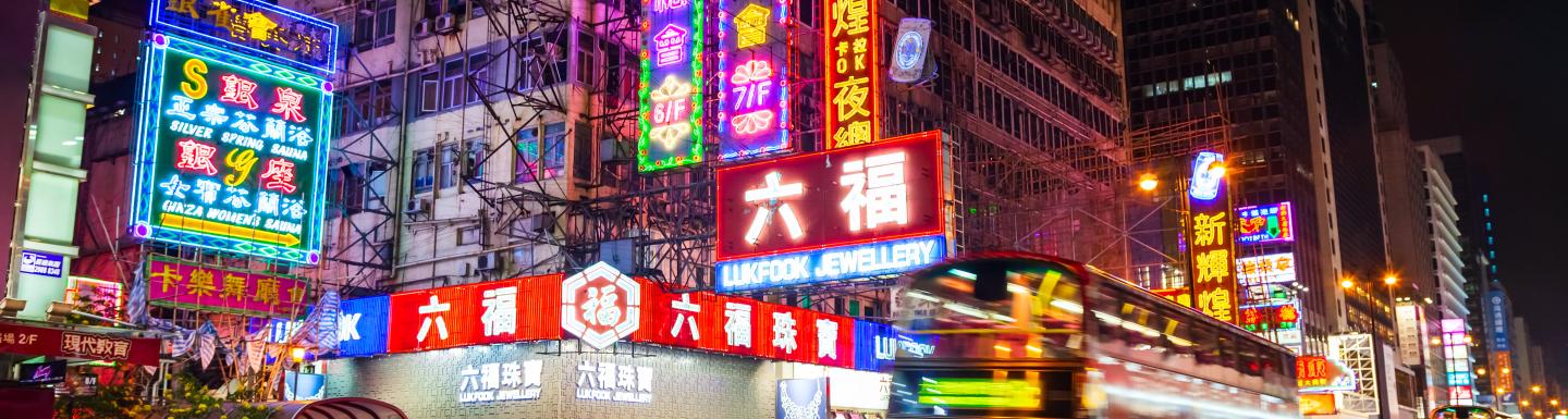 Cityscape at night, neon signs, bus rushing past