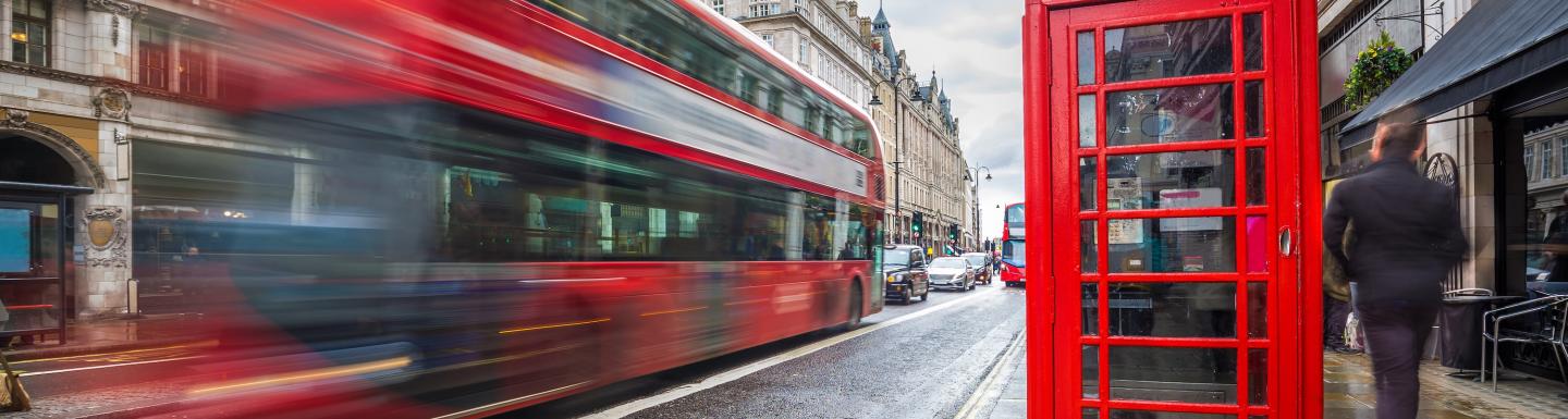 A blurred red double decker bus with a red telephone booth on the right side