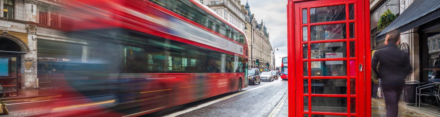 A blurred red double decker bus with a red telephone booth on the right side