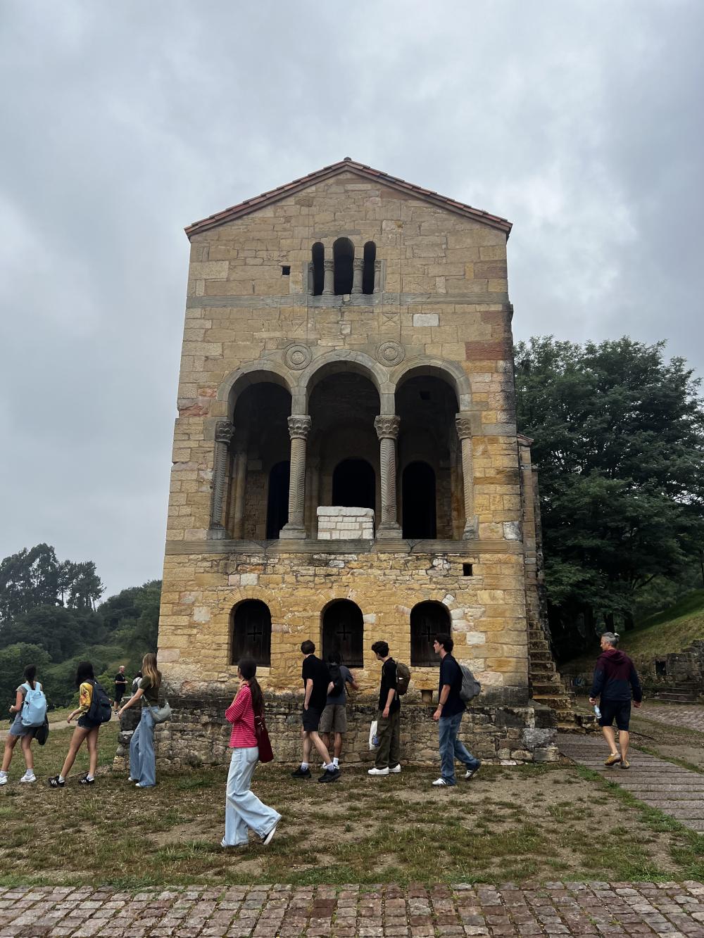 Students walking to the left in front of a stone building