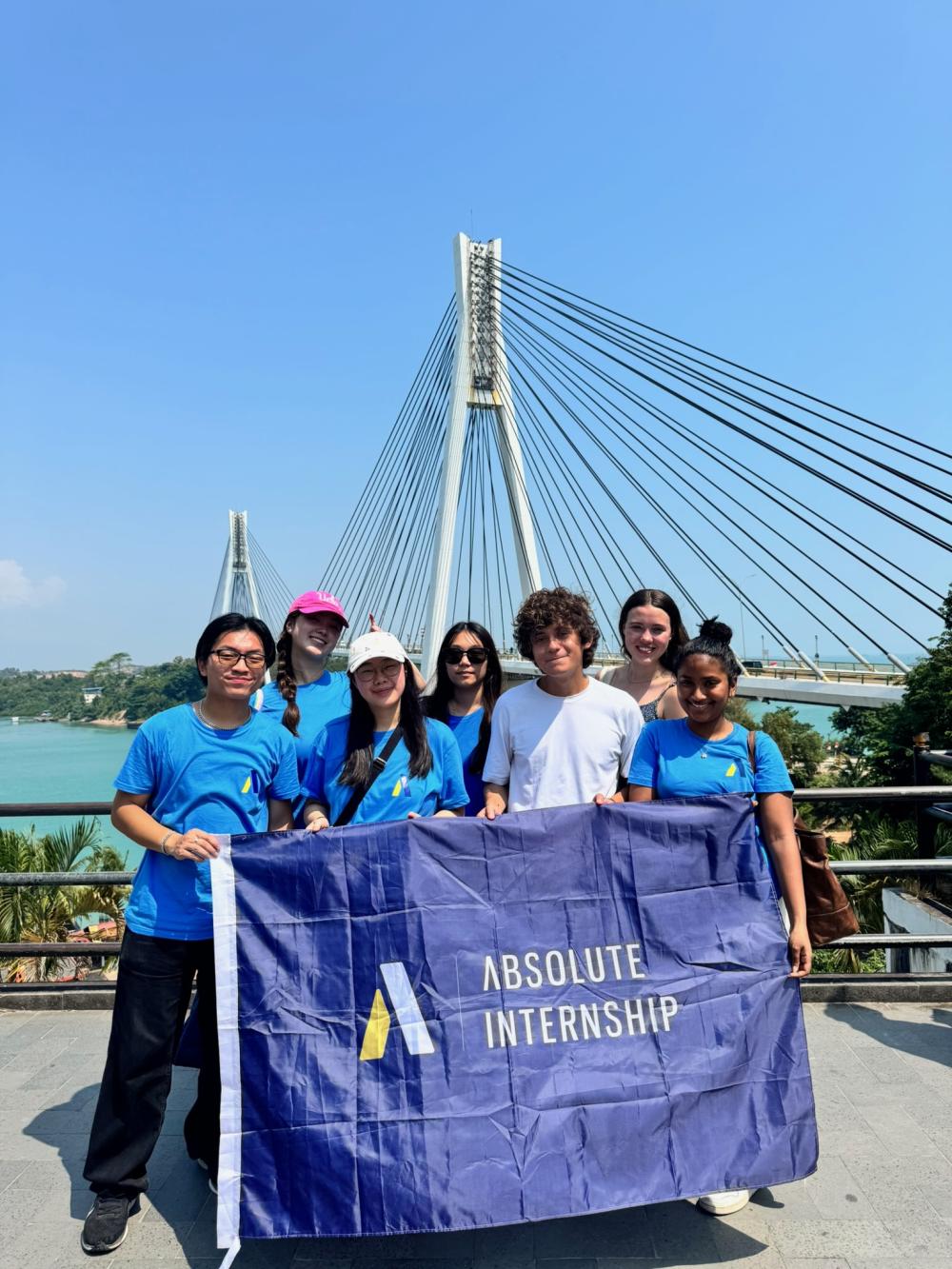 A group of students standing in front of a bridge holding a blue flag