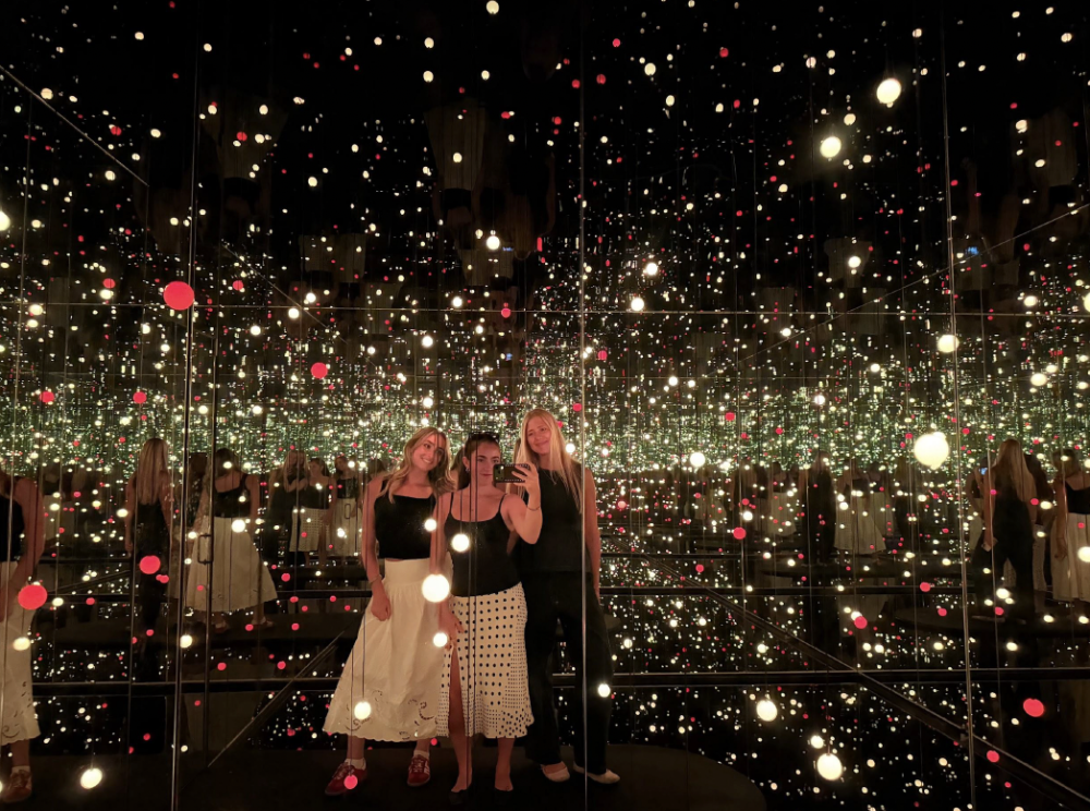 Three students standing in a dark room with white and red dotted lights