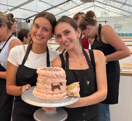 Two UO students in black aprons holding a pink cake