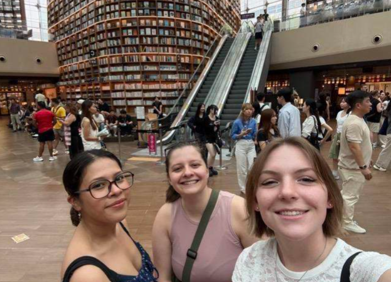 Three students posing in front of a book wall