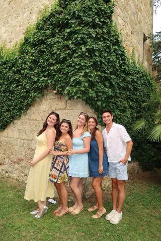 Five students smiling for a photo by a cobblestone building covered in vines