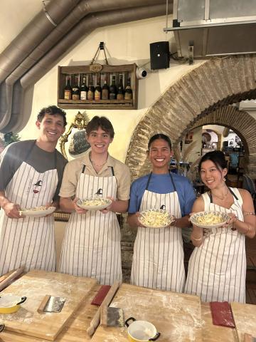 Four students holding up plates of homemade pasta in Italy