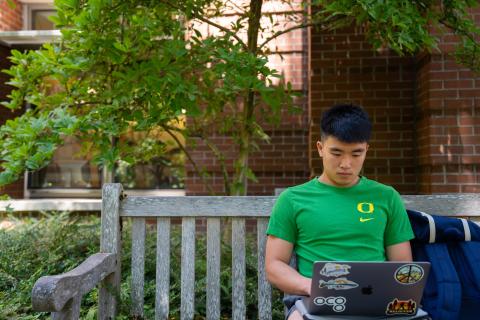 UO student working on a computer while sitting on a bench on campus