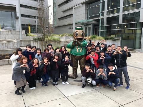 Group of students "throwing their o" in front of a Duck statute