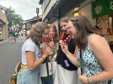 Four girls eating strawberries on a stick in a Japanese market.