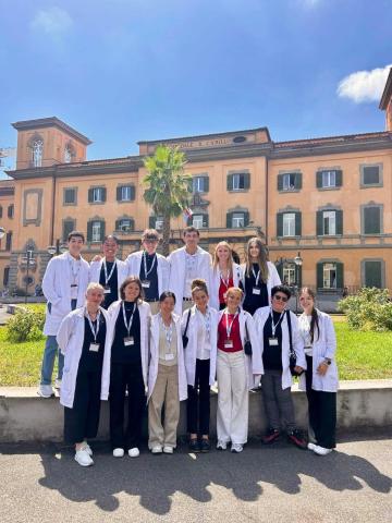 Cohort of premed students smiling outside an Italian hospital wearing lab coats and name tags