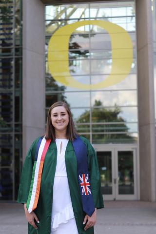 Woman standing in car and gown with graduation sashes