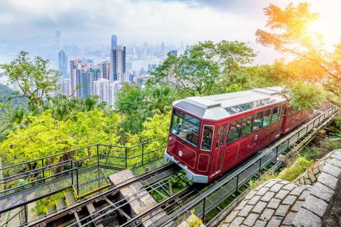 Red train on tracks on side of hill with city skyline in the background