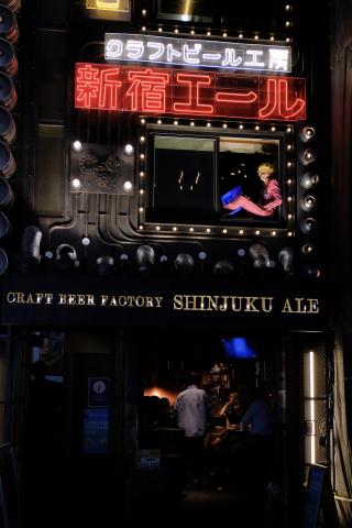 photo is dark, someone in a pink jumpsuit sits in a window with the word "Shinjuku" below