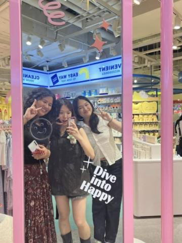 Megan and two friends are posing in the reflection of a mirror at the mall
