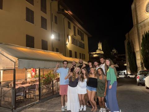 Luke stands with 10 other students, holding up peace signs and smiling outside of a restaurant at night