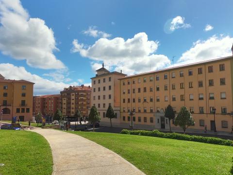 A concrete path amongst grass with a large building in the background against a blue sky with white clouds