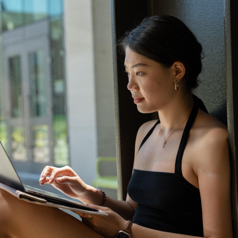 An international student sitting next to a window working on a computer