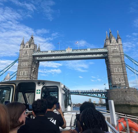 View of Tower Bridge in London with a clear blue sky, featuring tourists taking photos from a nearby location.