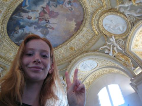 Selfie of student Emma Egbert holding a peace sign, posing in front of a painted ceiling