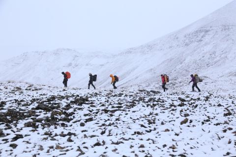 five students with heavy coats and backpacks hike in the rocky snow