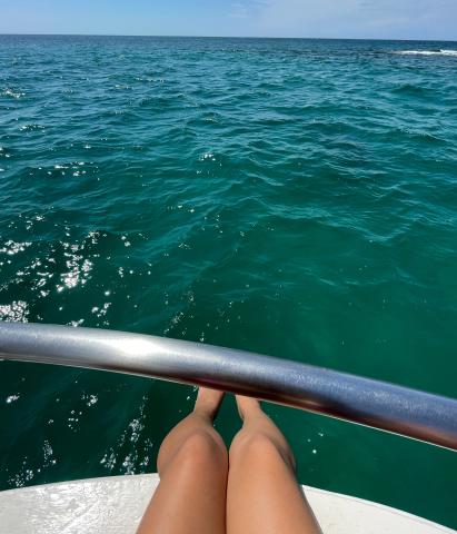 A view from a boat looking out over the ocean with a person's legs visible, resting on the edge under a railing.