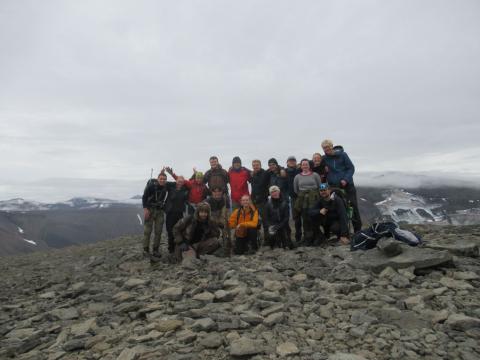 a group of students stand on a hilltop of rocks; snow and clouds are in the background