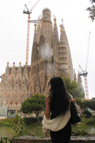 A person observes the Sagrada Familia in Barcelona, under construction with cranes visible.