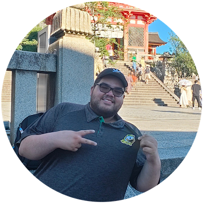 College student pointing to the University of Oregon mascot mark on his polo, standing in front of a temple in Japan