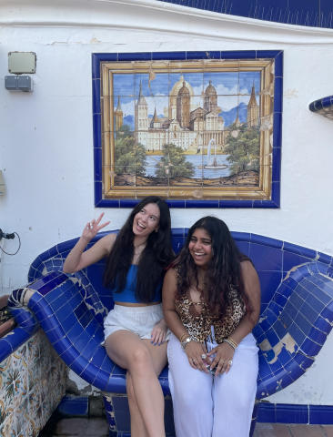 Two people sit on a blue tiled bench. They are smiling and looking at the camera.