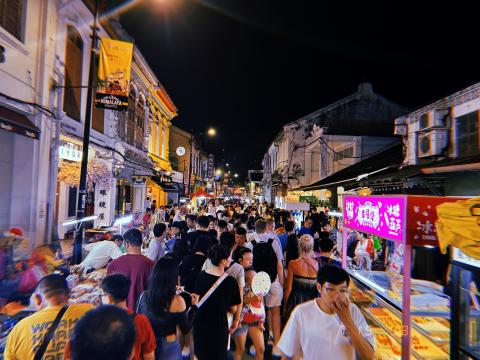 Crowds of people in a narrow street at night, lit by food stalls on both sides