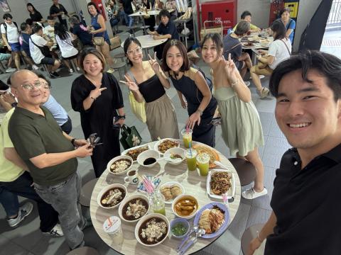Logan and five other people stand around a circular table with plates of food and pose