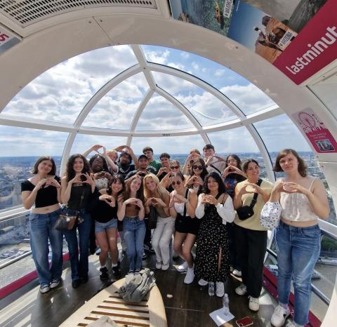 Large group of college students in the London eye holding up an "O" sign with their hands. 