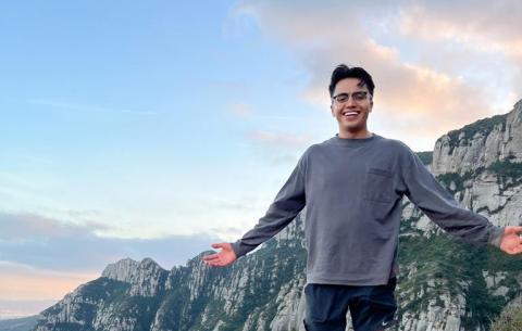 Link to distinguished scholarships. Image description: a young man with arms stretched wide posing in front of a mountain