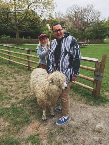 Young man pets a sheep with a shepherd standing behind him