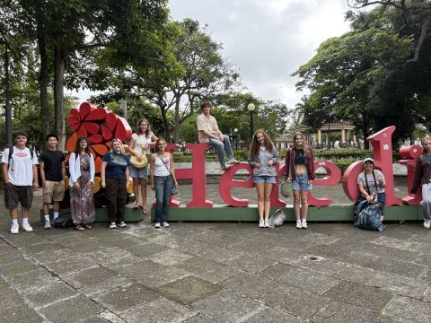 Ten people stand around a large red sign that says "Heredia"