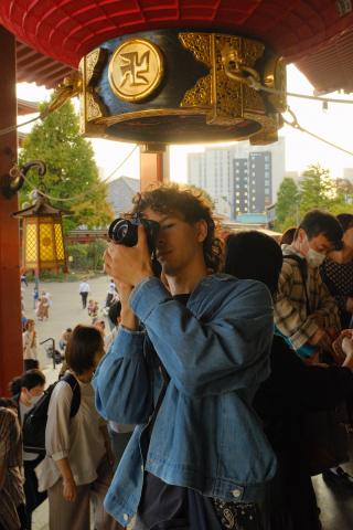 Student holding a camera and looking through the viewfinder and looking at the camera
