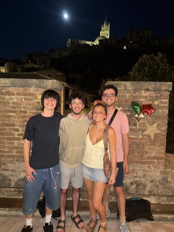 4 students stand in front of a wall outside, it is dark