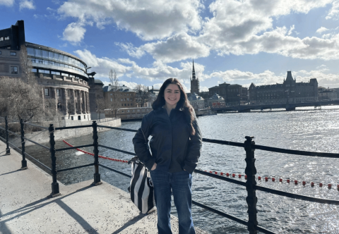 Student smiling by a river in Stockholm, Sweden under a partly cloudy sky