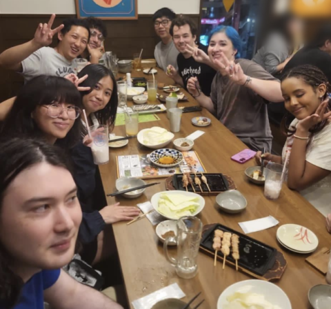 9 people are seated at a long dinner table in a restaurant, posing for the camera