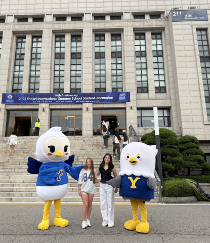 Megan and her roommate stand outside a big academic building and pose with two birds, the Yonsei mascots