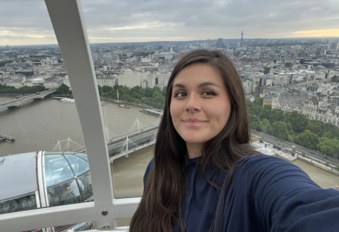 Nathalie poses for a selfie in a clear ferris wheel, with the city skyline of London below