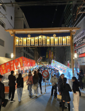 a gate above the street is illuminated by lights; people are walking underneath it