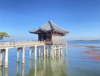 a small temple rests on pillars above the water, a boardwalk connects to the temple and leads out of the left frame