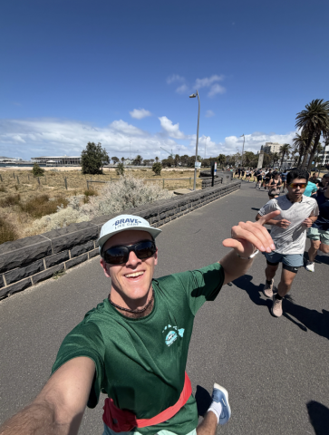 Calvin, in running clothes, sunglasses, and a hat, takes a selfie with a trail of runners behind him