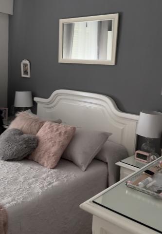 White bed frame with light grey blanket in a bedroom with grey walls 